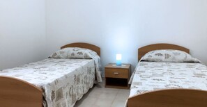 Una camera da letto con due letti singoli, ognuno dotato di una testiera in legno e una coperta a motivi decorativi. Tra i letti si trova un comodino con una lampada.
