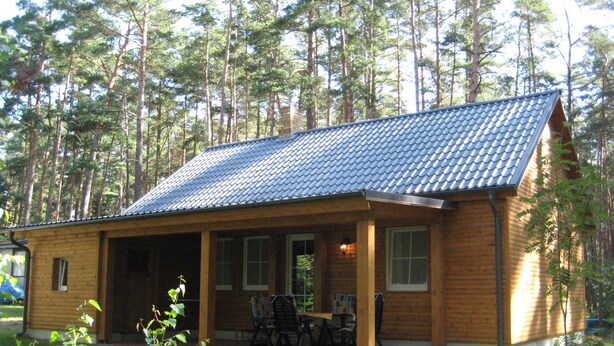 Eine Holzhütte mit Ziegeldach, einer Veranda und einem kleinen Tisch mit St ühlen.