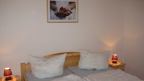 Ein Schlafzimmer mit einem Holzkopfteil, zwei weißen Kissen, einer weißen Bettdecke, einem Nachttisch mit Lampe und einem gerahmten Bild an der Wand.