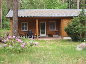 A wooden cabin with a porch, a table, and chairs.