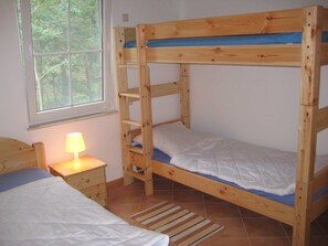 A bunk bed with a ladder, a bedside table with a lamp, a window with a view of trees, and a striped rug on the floor. - Holiday house 2 - Dependance holiday houses at the Kastavensee (Lychen)
