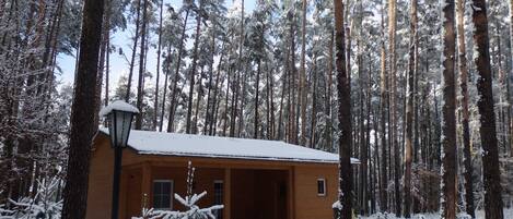 Eine Holzhütte, umgeben von hohen, mit Schnee bedeckten Bäumen.