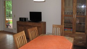 Ein Essbereich mit einem Tisch, Stühlen, einem Fernseher auf einer Holzkommode und einer Kommode mit Glastüren.