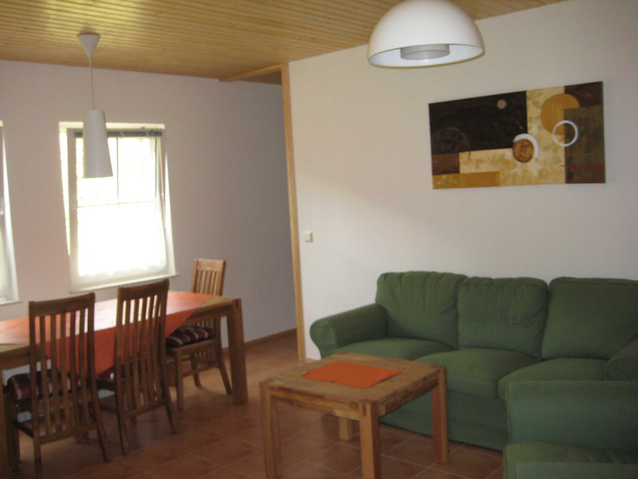 Ein Essbereich mit Tisch und Stühlen, einem grünen Sofa und einem Bild an der Wand.