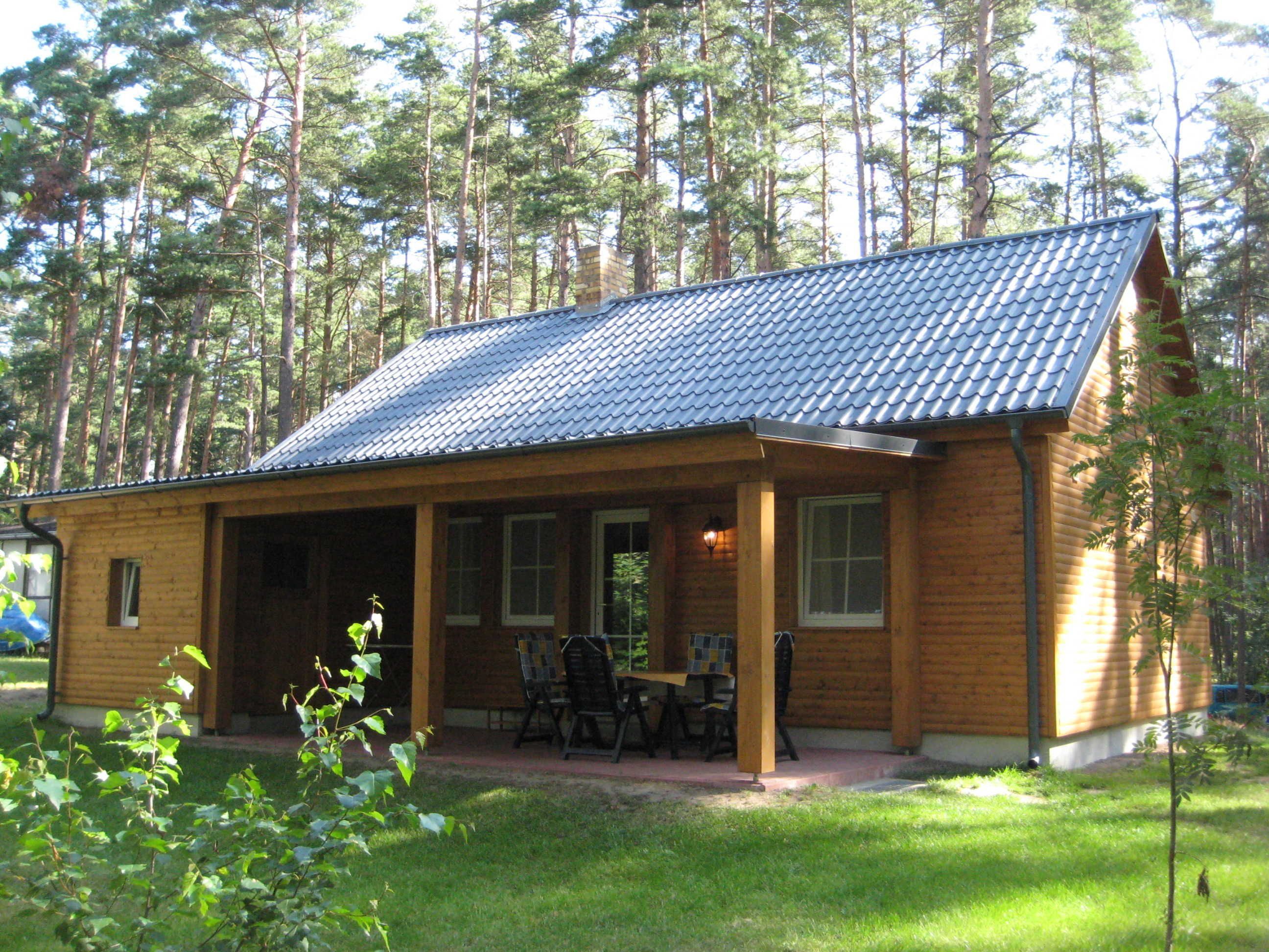 En træhytte med tegltag, en overdækket veranda og et lille bord med stole.