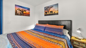 Ein Schlafzimmer mit einem Bett, gemusterten Betttextilien, einem Nachttisch mit Lampe und zwei an der Wand befestigten Elefantenbildern.
