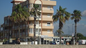 Un immeuble à plusieurs étages doté de balcons, une enseigne indiquant « La Frescura », et des palmiers.