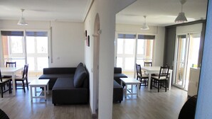Un salon moderne avec un canapé de couleur sombre, une table à manger avec des chaises et un coin cuisine visible à travers une porte ouverte.