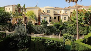 A multi-story residential building with a tiled roof, surrounded by well-maintained gardens and palm trees. - Valparaiso Apartment Burriana Beach (Nerja)