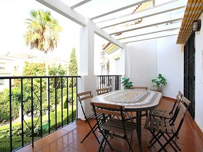 A balcony with a tiled floor, a round table with chairs, and a potted plant.
