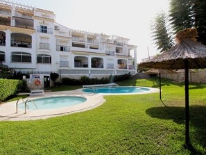 A hotel with two swimming pools, a thatched-roof structure, and a well-maintained lawn.