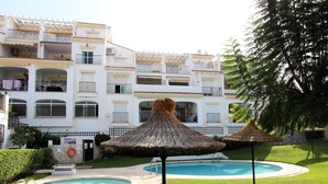 A hotel with a pool area, including two thatched umbrellas and a well-maintained lawn. - Valparaiso Apartment Burriana Beach (Nerja)