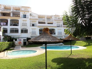 A hotel with a pool area, including two thatched umbrellas and a well-maintained lawn.