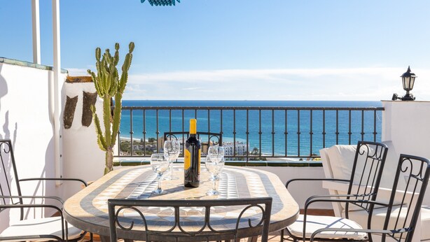 Une table ronde entourée de chaises, une bouteille et des verres, le tout sur une terrasse offrant une vue sur la mer.