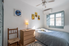 Un dormitorio con cama, cómoda de madera, silla, ventilador de techo y decoración en la pared.