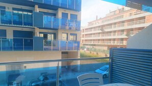 A balcony with a table and chairs, overlooking a street with parked cars and a building with multiple balconies. - Miralcielo 2ºA- LEK (Peñiscola)