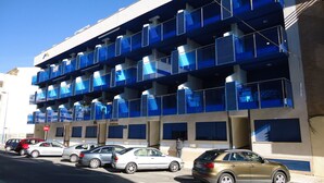 A multi-story parking garage with blue balconies and a row of parked cars. - Miralcielo 2ºA- LEK (Peñiscola)