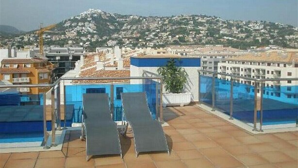 A rooftop pool area with lounge chairs and a view of a cityscape in the background. - Miralcielo 2ºA- LEK (Peñiscola)