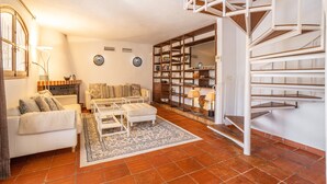 Una sala de estar con un sofá blanco, una mesa de centro, una alfombra, una escalera y una estantería.