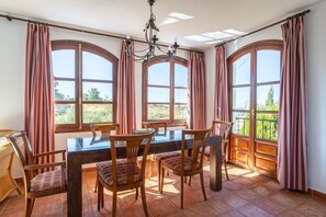 A dining area with a table, chairs, and large arched windows with curtains.