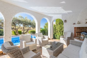 A covered outdoor seating area with wicker furniture, a fireplace, and a view of a pool and trees.