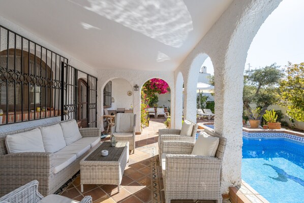 An outdoor patio with wicker furniture, a pool, and white columns.