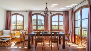 Un comedor con una mesa y sillas, ventanas amplias con cortinas, y vistas al exterior.
