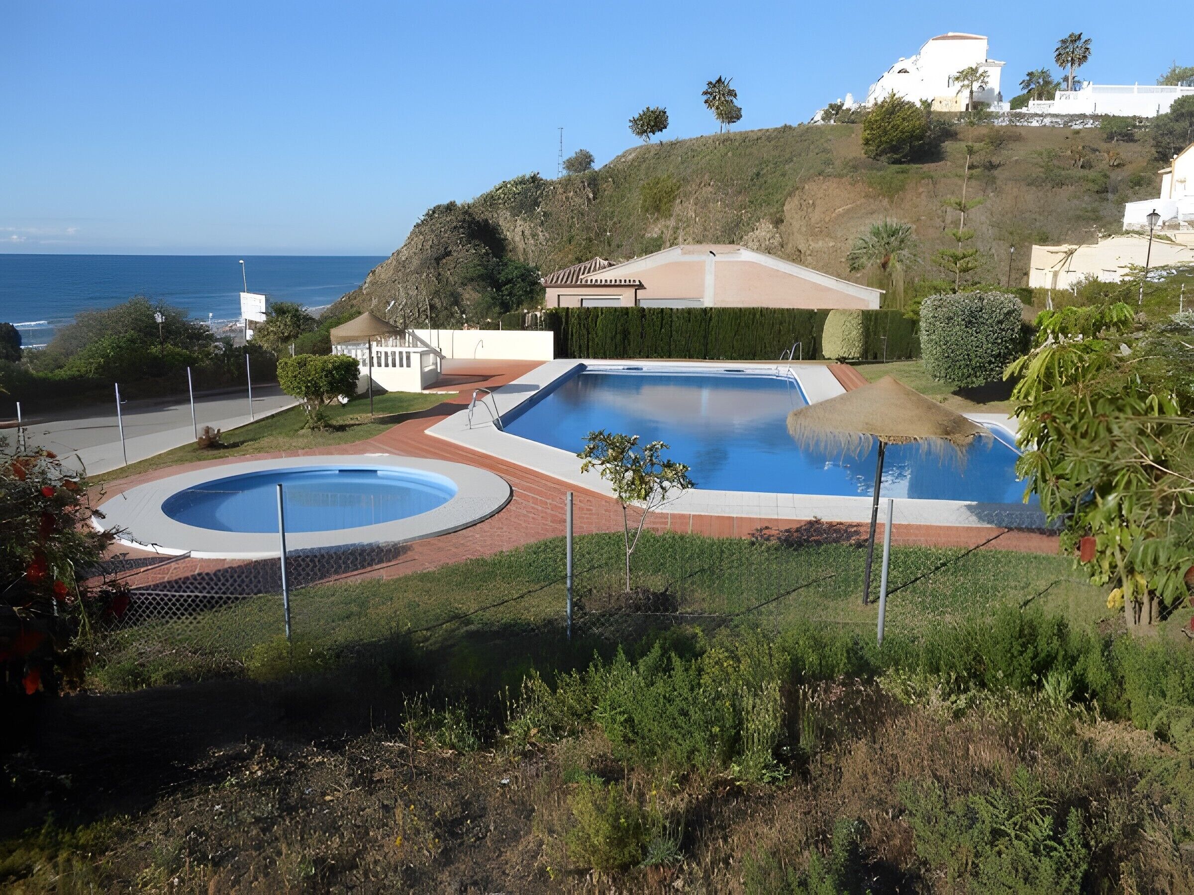 A residential area with a swimming pool, a view of the ocean, and a hillside with vegetation.
