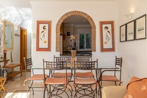 Uma área de refeições com mesa de vidro, seis cadeiras e um arco de tijolos.