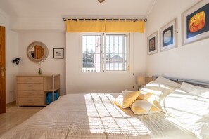 Quarto com cama, penteadeira, janela com cortinas e quadros na parede.
