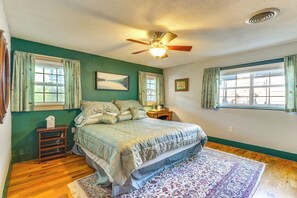 A bedroom with a bed, two windows with curtains, a ceiling fan, and a nightstand with a lamp. - Walk to Mueller Lake Park! Home w/ Patio & Yard (Austin)