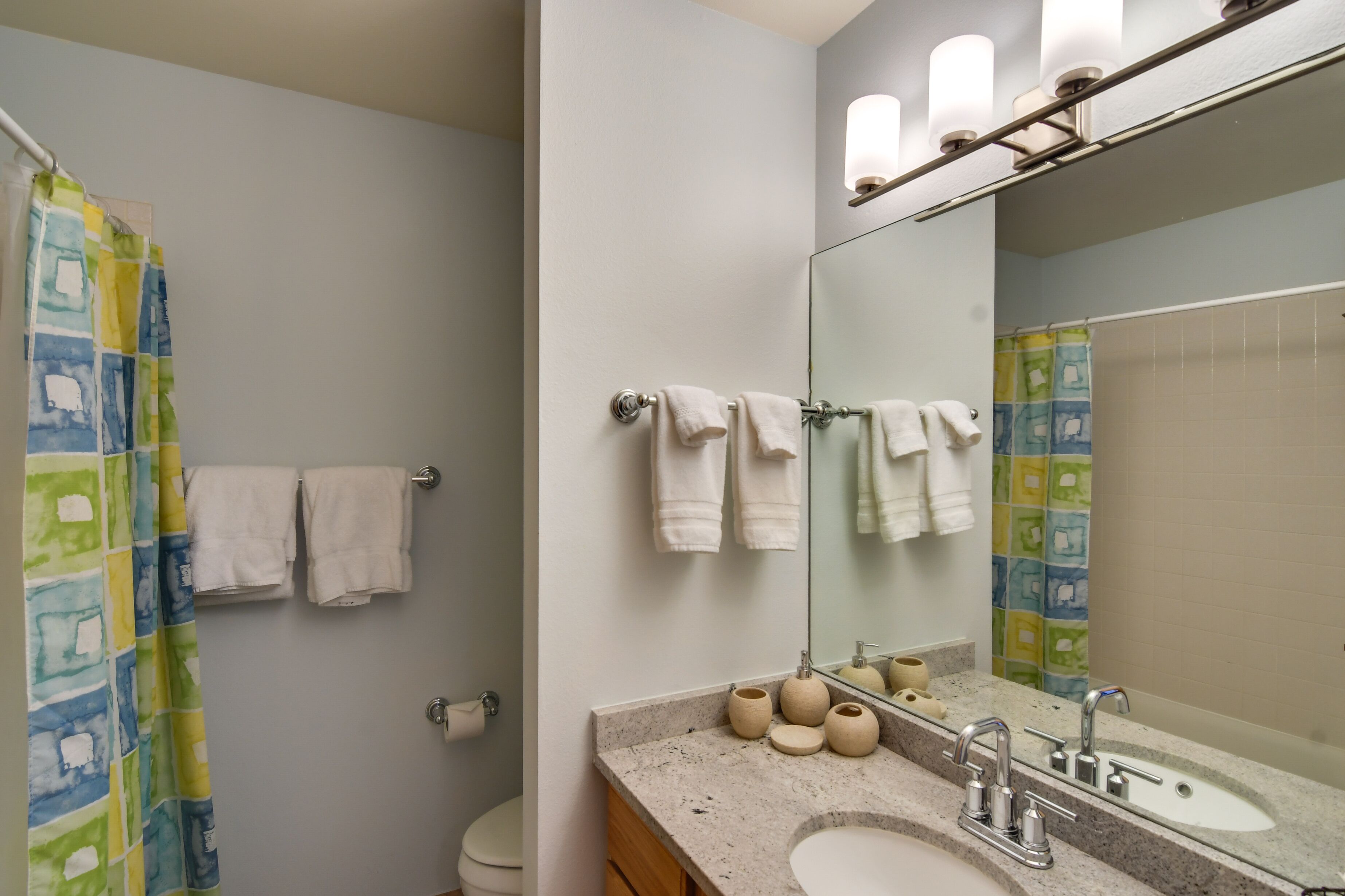 A bathroom with a shower curtain, a toilet, a sink with a mirror, and a towel rack.