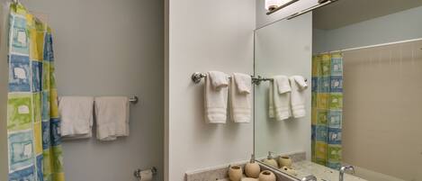 A bathroom with a shower curtain, a toilet, a sink with a mirror, and a towel rack.