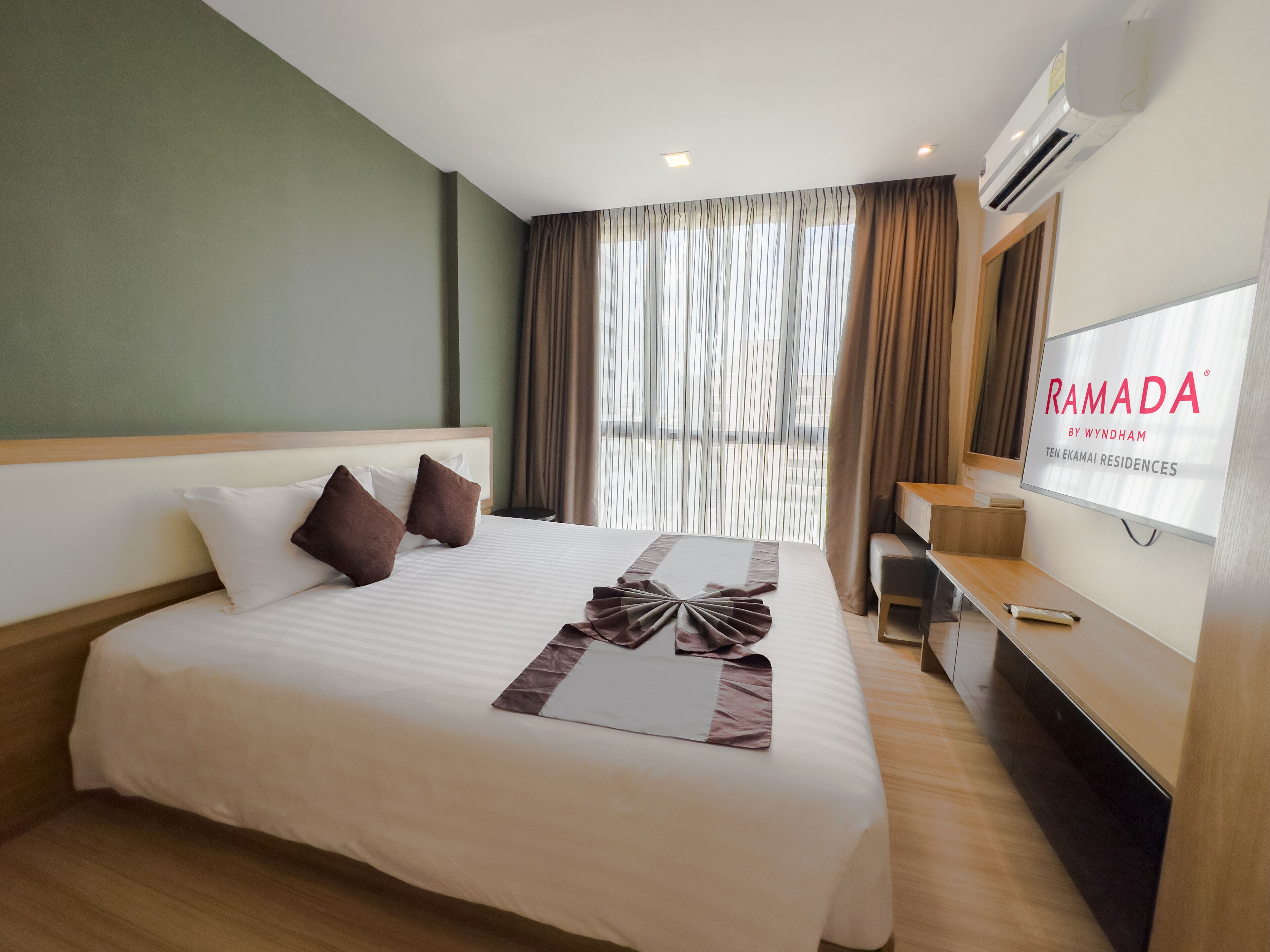 Une chambre d’hôtel avec un grand lit, une télévision et une fenêtre avec des rideaux.