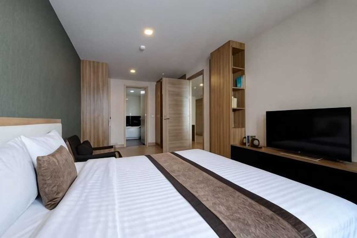 A hotel room with a large bed, a TV, a wardrobe, and a desk.
