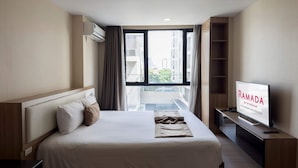 Een hotelkamer met een bed, een televisie en uitzicht op gebouwen door een raam.