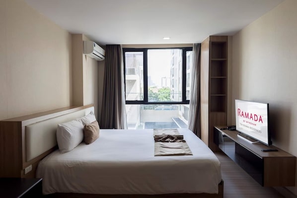 A hotel room with a bed, a TV, and a view of buildings through a window.