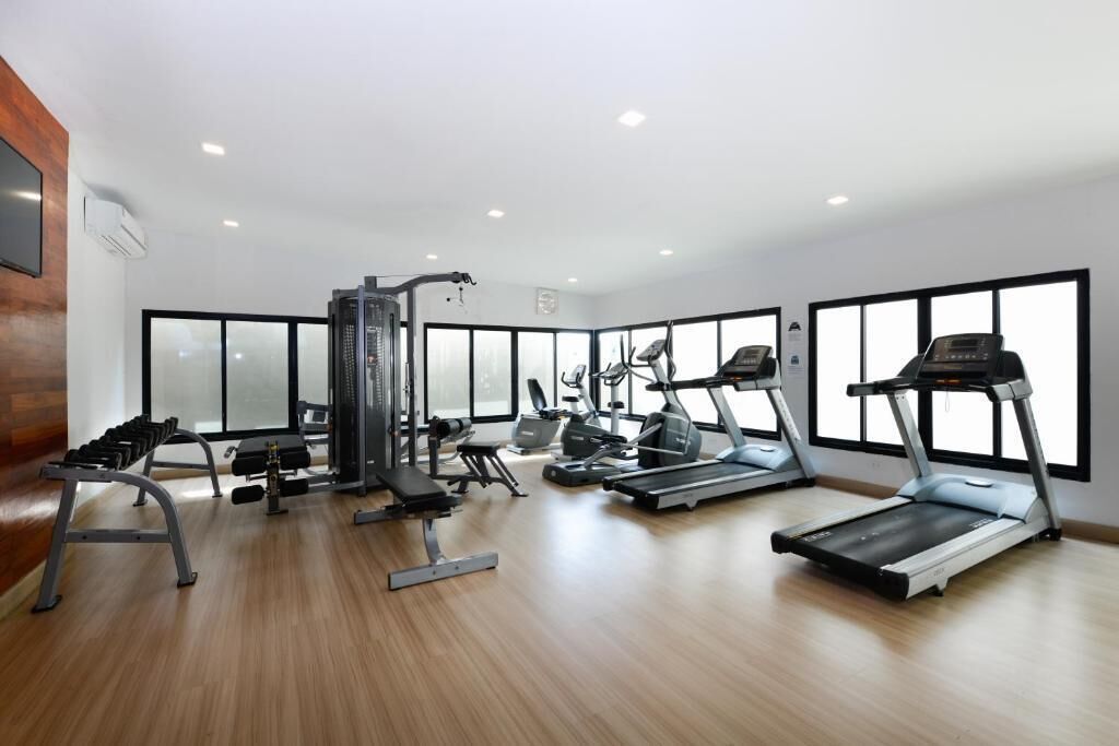 A modern gym with cardio machines, weight stations, and a wooden floor.