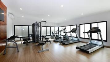 A modern gym with cardio machines, weight stations, and a wooden floor.