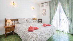 Ein Hotelzimmer mit Bett, Nachttisch, Lampe, Klimaanlage und Vorhängen.