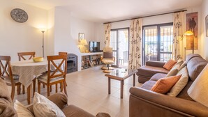 Ein Wohnzimmer mit einer Couch, Sesseln, einem Esstisch, einem Kamin und einem Fernseher.