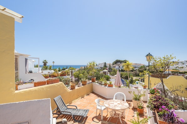 A rooftop terrace with a view of the sea, potted plants, and outdoor furniture.