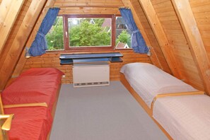 Une petite chambre mansardée, chaleureuse et accueillante, avec deux lits simples, une fenêtre avec des rideaux et un radiateur.