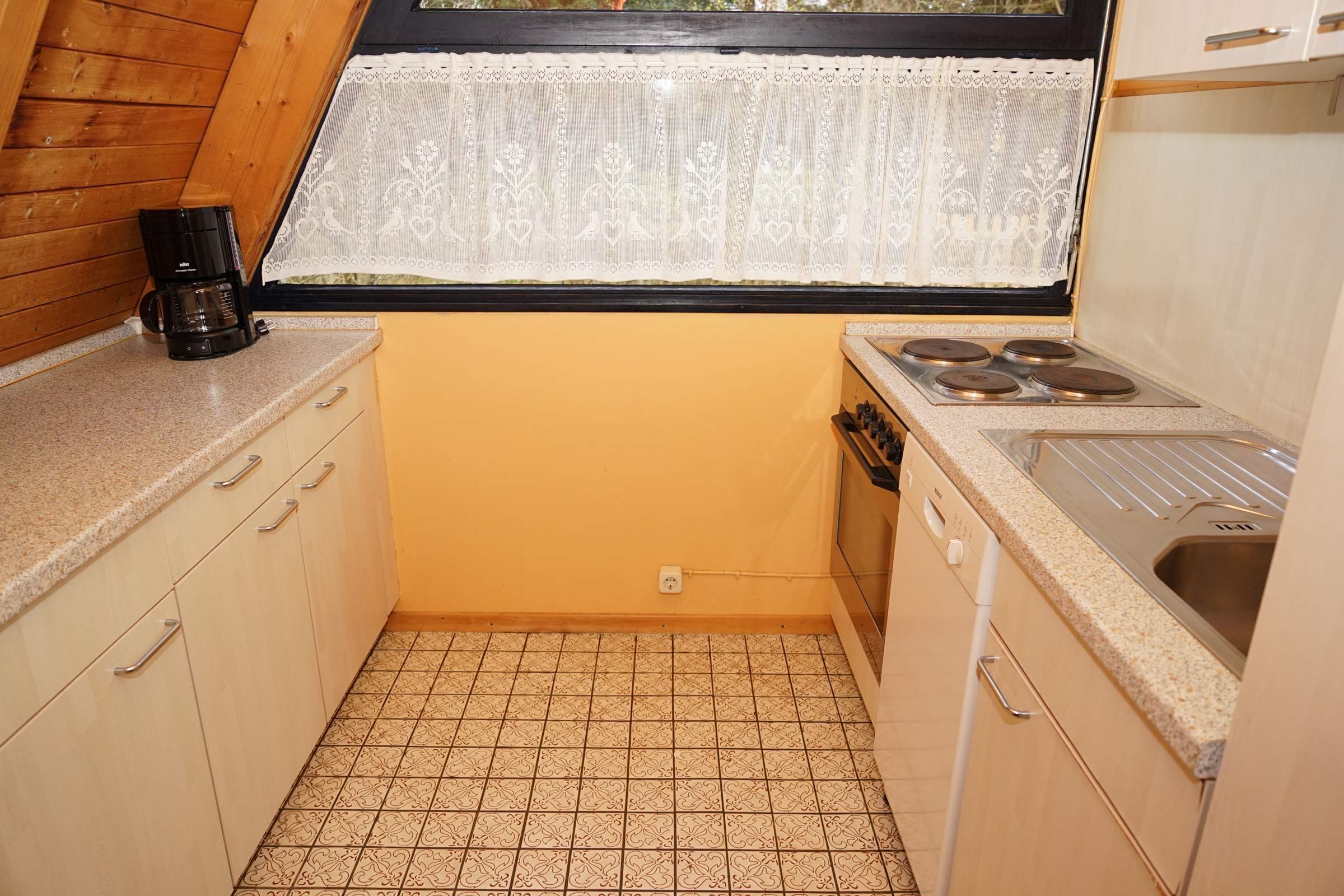 A compact kitchen with a window, a coffee maker, a stove, and a sink.