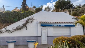 Um bar de lanches com fachada branca, toldo azul e parede revestida de azulejos.