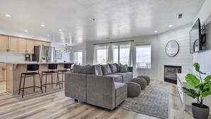 Ein modernes Wohnzimmer mit grauem Sofa, Holzboden und einem großen Fenster mit Blick.