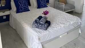 Een netjes opgemaakt bed met wit en blauw beddengoed, een blauw hoofdbord en een nachtkastje met een lamp.