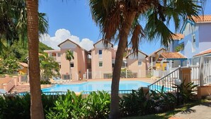 Een resort met een zwembad, palmbomen en een gebouw met een pannendak.