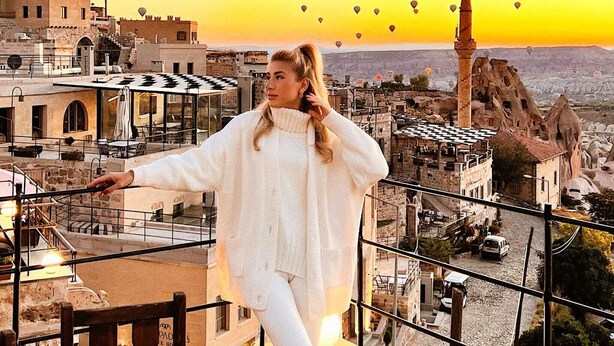 A person standing on a rooftop terrace with a table set for dining, overlooking a cityscape with traditional architecture and a prominent minaret. - Peristyle Cave Cappadocia - Special Class (Nevsehir)