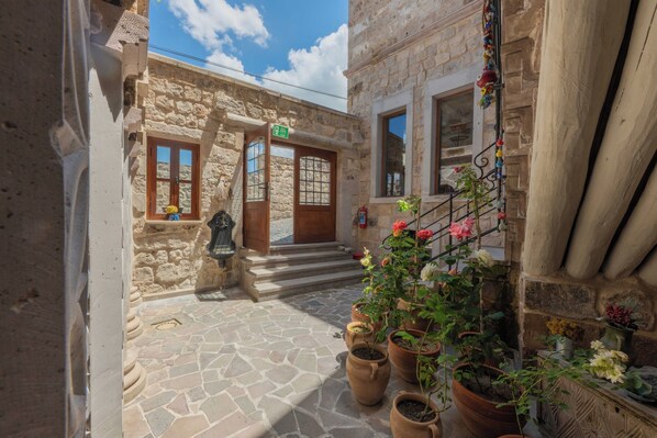 A stone building with a wooden door, a small porch with potted plants, and a stone-paved courtyard. - Peristyle Cave Cappadocia - Special Class (Nevsehir)